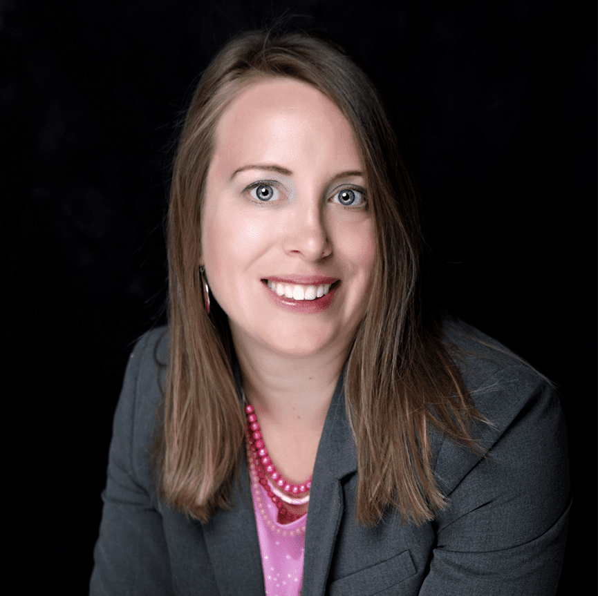 A woman in a suit and pink shirt smiling.