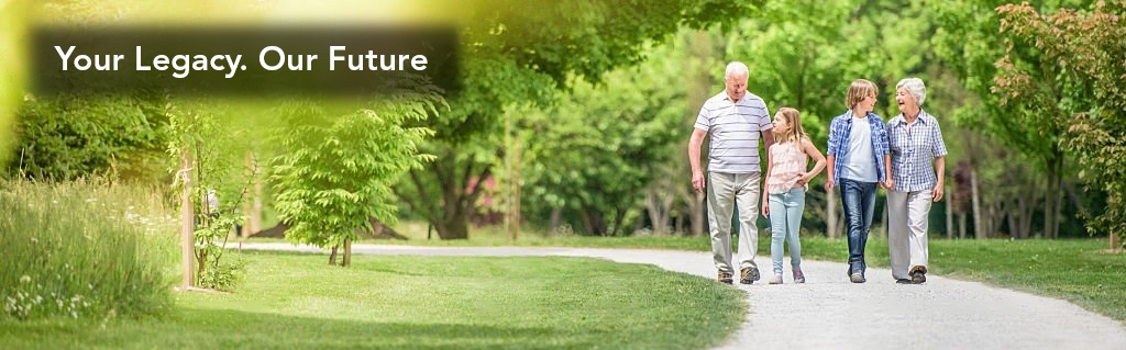 A man walking down the sidewalk in front of trees.